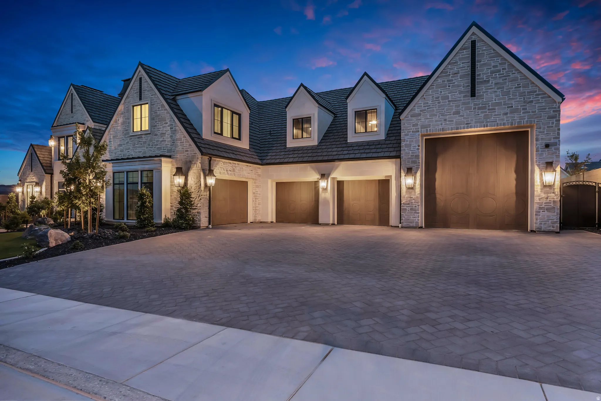Stone and stucco exterior featuring multiple gables, dormer windows, and a multi-car garage