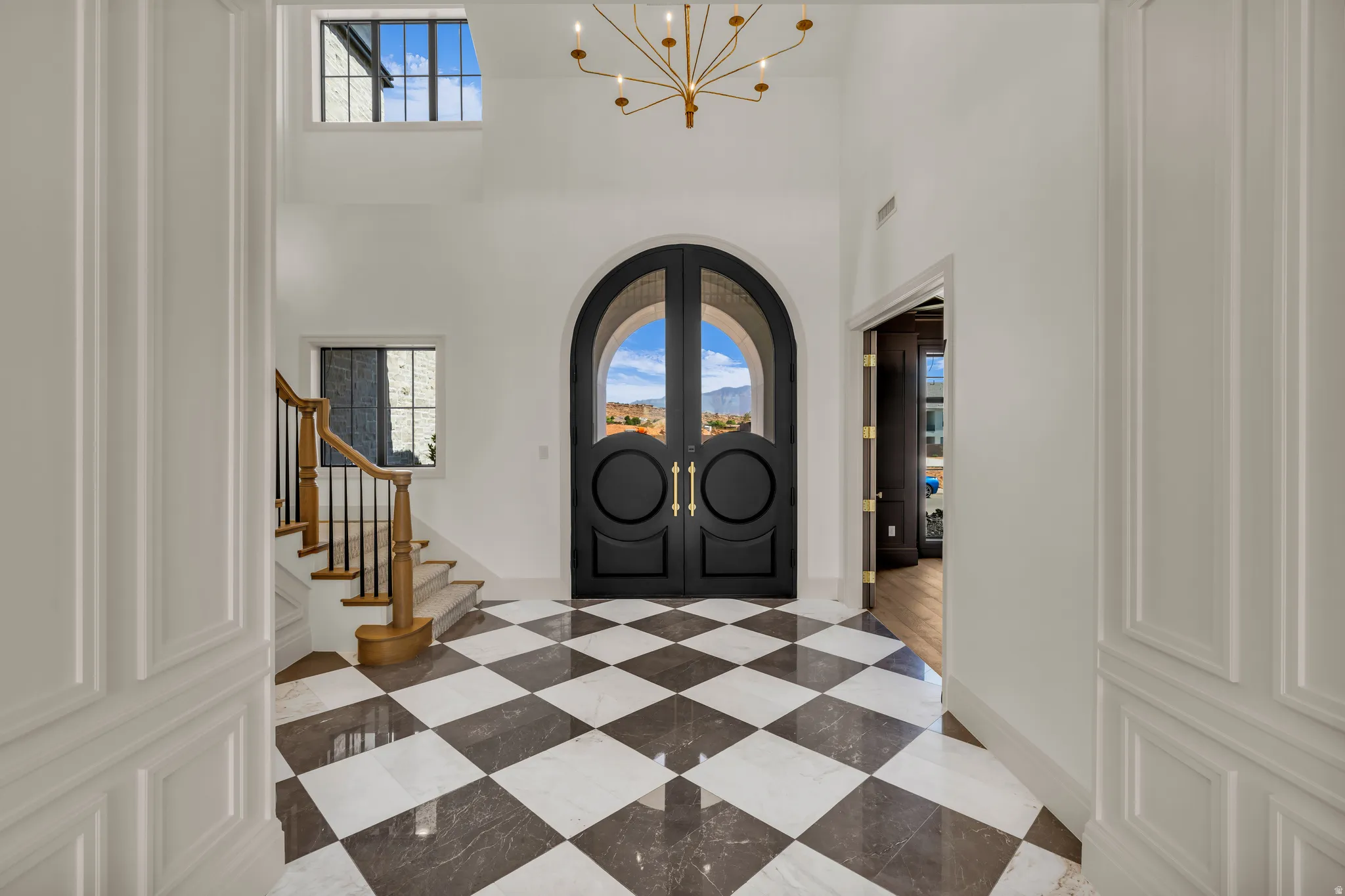 Grand entry foyer featuring checkerboard tile flooring, a prominent arched double-door entry, and a high ceiling with a gold-tone chandelier