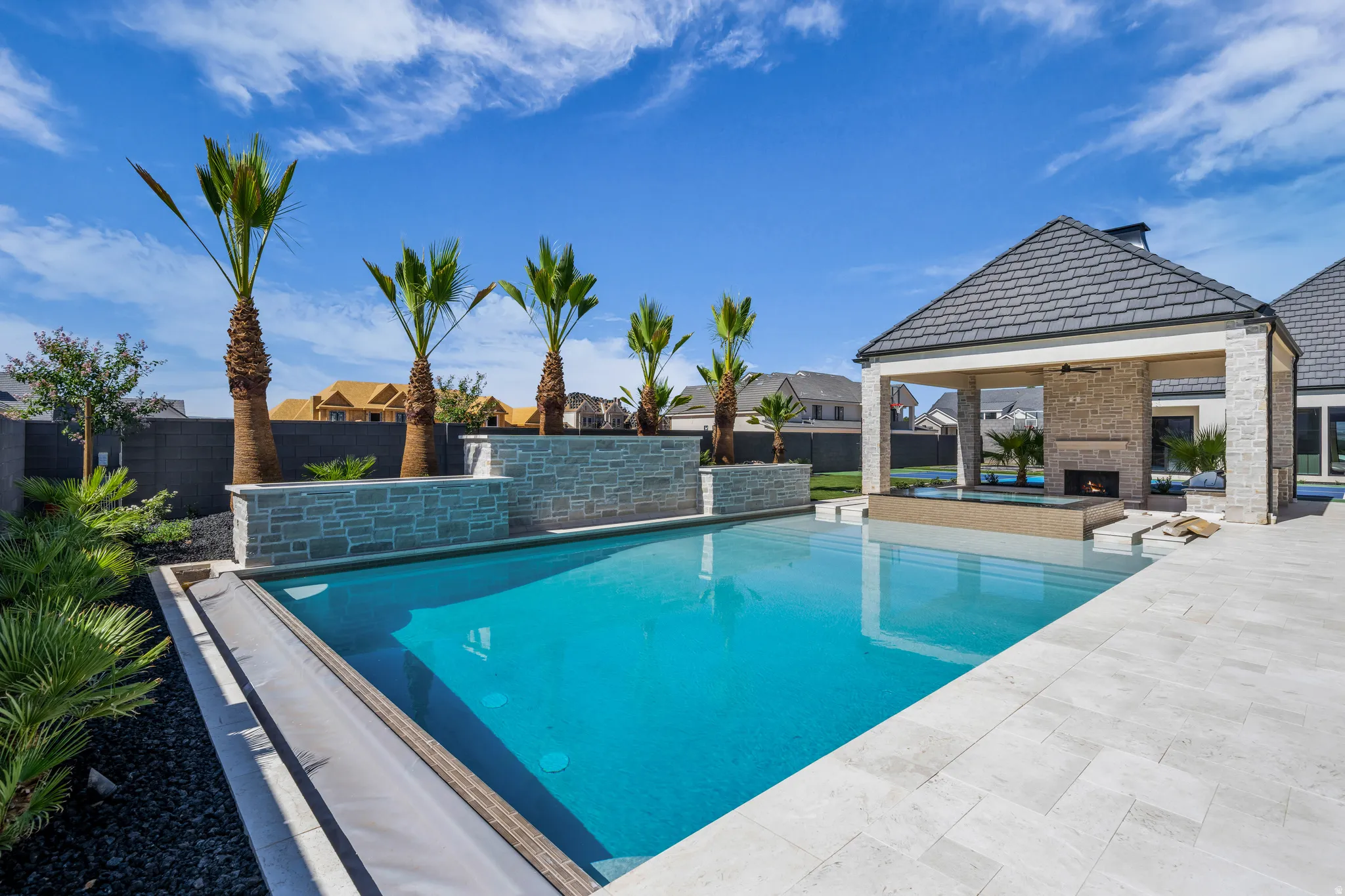 Resort-style backyard featuring a swimming pool, integrated spa, and a covered patio with a stone fireplace