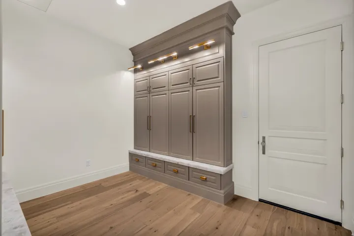 Built-in cabinetry with ample storage, integrated lighting, a marble-look countertop, brass hardware, and wood-finish flooring
