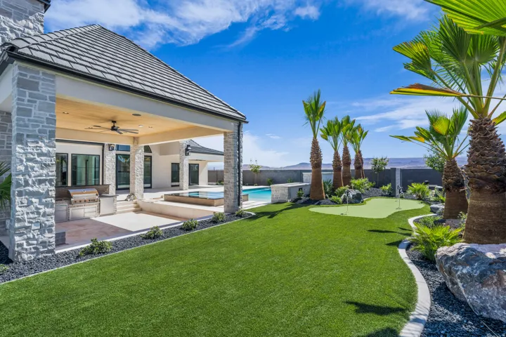 Expansive exterior showcasing a covered patio with built-in grill, a putting green, mature palm trees, and a swimming pool with an integrated spa