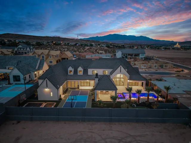 Contemporary residence featuring a dark tile roof, multiple dormer windows, a spacious backyard with a lighted pool, an outdoor covered patio, and a dedicated sport court