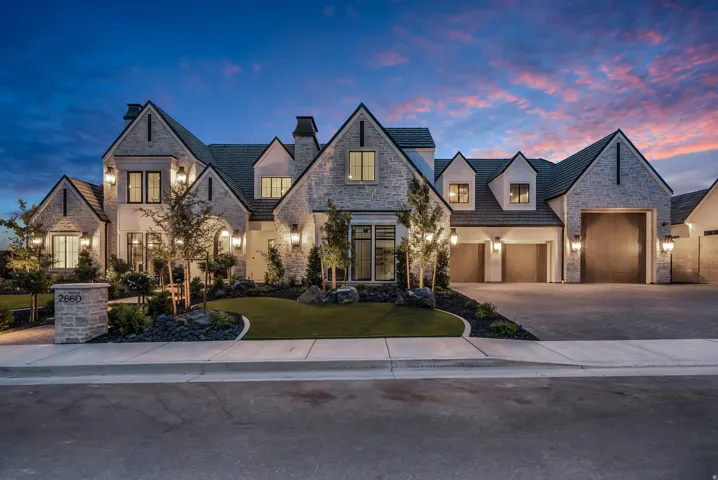 Stone façade residence featuring multiple gables, a paved driveway, and an integrated multi-car garage with wood-finish doors
