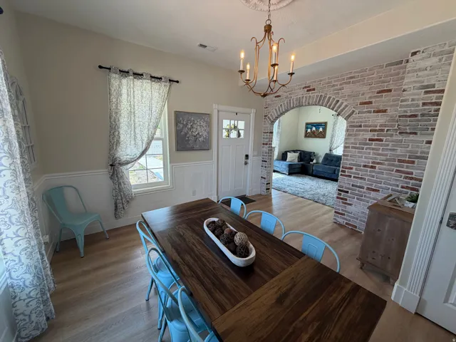 Dining area featuring wood-finish flooring, wainscoting, an arched brick entryway, and a decorative chandelier