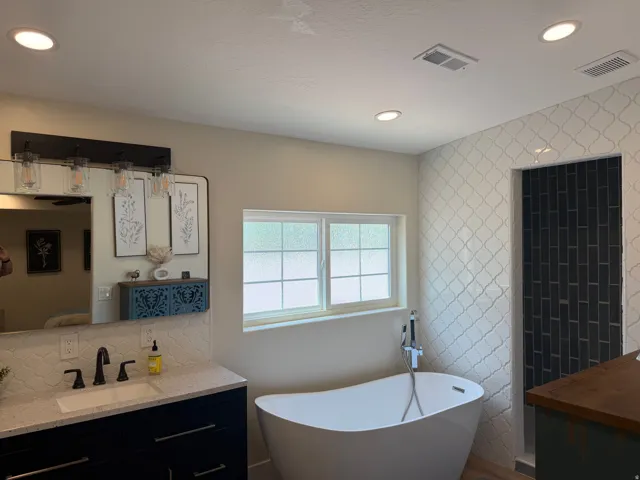 Modern bathroom featuring a freestanding soaking tub, a shower with dark subway tile, an elegant vanity with a white countertop and undermount sink, and recessed ceiling lighting