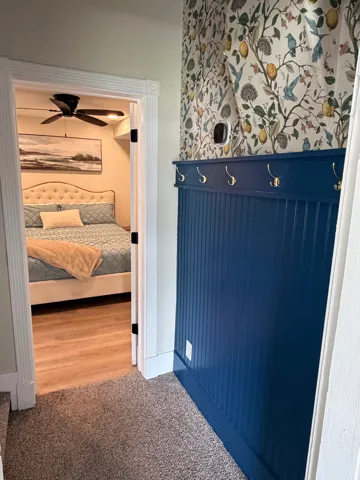 Entryway featuring a decorative accent wall with botanical wallpaper, beadboard paneling, and brass coat hooks