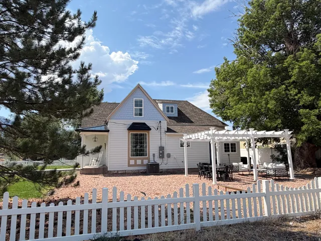 White picket fence enclosing a gravel yard with a large patio featuring a white pergola