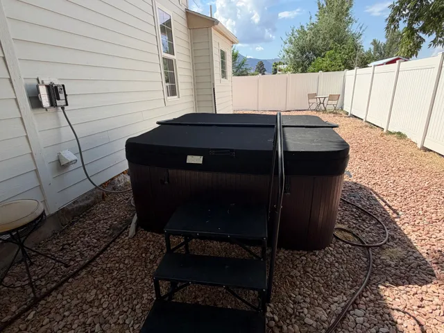 Private outdoor space featuring a covered spa, rock landscaping, and white vinyl perimeter fencing
