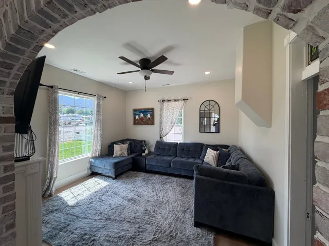Inviting living area featuring a decorative brick archway, recessed lighting, a ceiling fan, a large window, and light wood-finish flooring