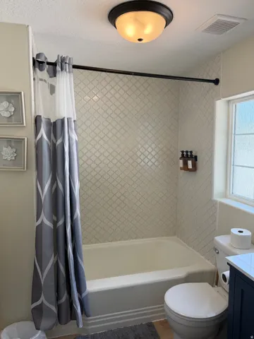 Bathtub with arabesque-patterned tile surround, recessed window, and flush-mount ceiling light