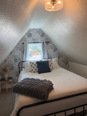 Room featuring sloped ceilings, patterned accent wall, recessed window with curtains, and a contemporary ceiling light fixture