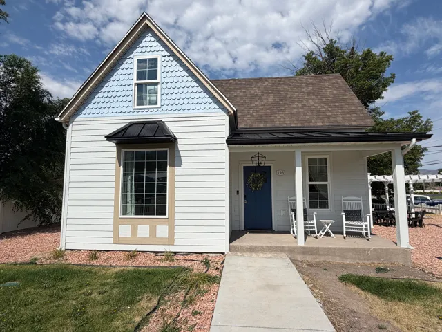 Charming exterior featuring white horizontal siding, a blue shingle-style gable accent, a welcoming front porch with white columns, a blue entry door, and a bay window with a black metal awning