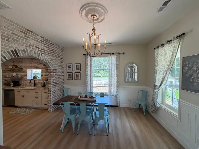 Open-concept dining area featuring wood-finish flooring, a decorative ceiling medallion with a chandelier, and wainscoting paneling