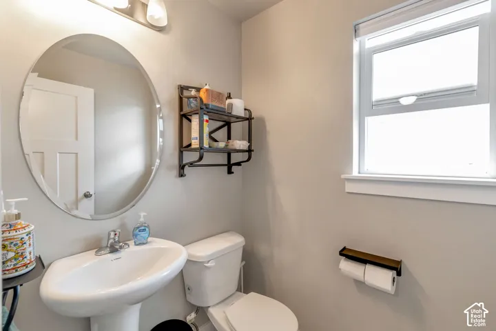 Pedestal sink with chrome faucet, oval mirror, and wall-mounted light fixture