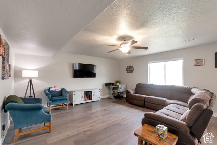 Spacious living area featuring wood-finish flooring, a ceiling fan with integrated lighting, a large window providing natural illumination, and recessed lighting