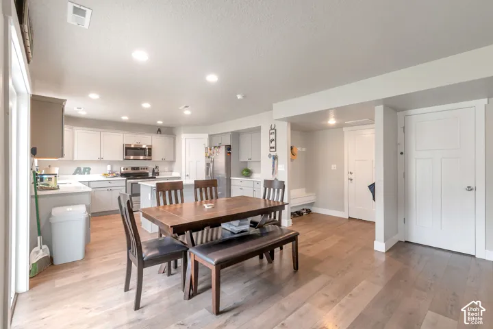 Open-concept living space featuring wood-finish flooring, a contemporary kitchen with light cabinetry, stainless steel appliances, and an island