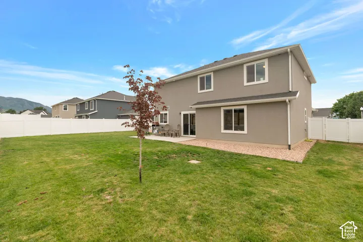 Spacious rear yard with a manicured lawn, a concrete patio, and a white vinyl fence
