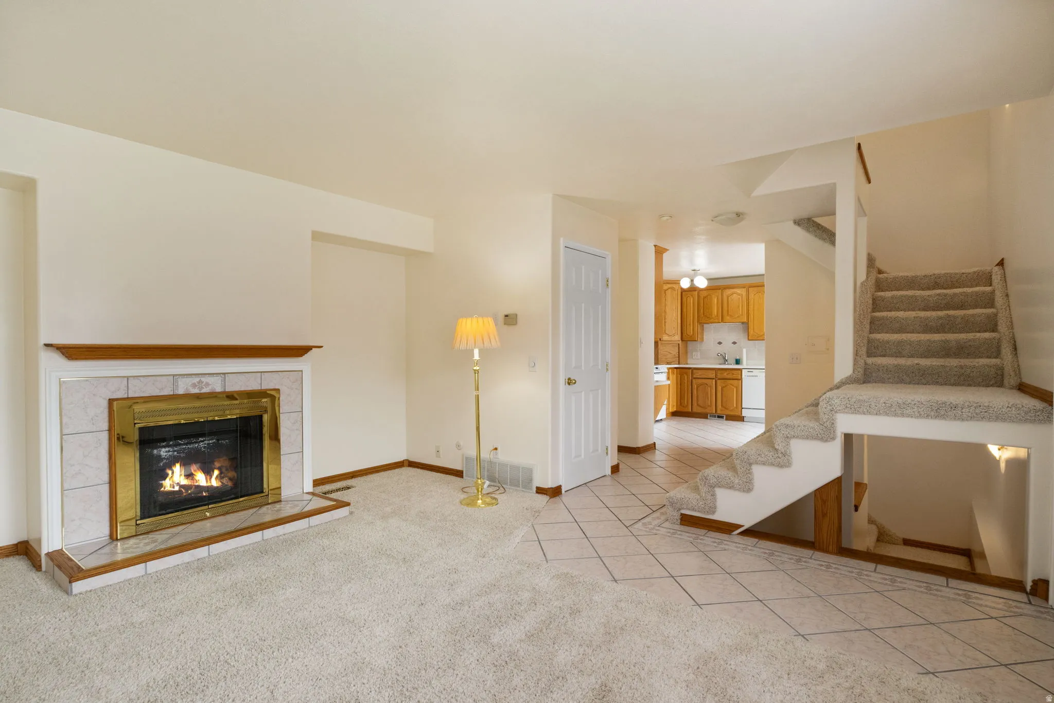 Living area with a tile-surround fireplace, light-toned carpeting, and a built-in staircase