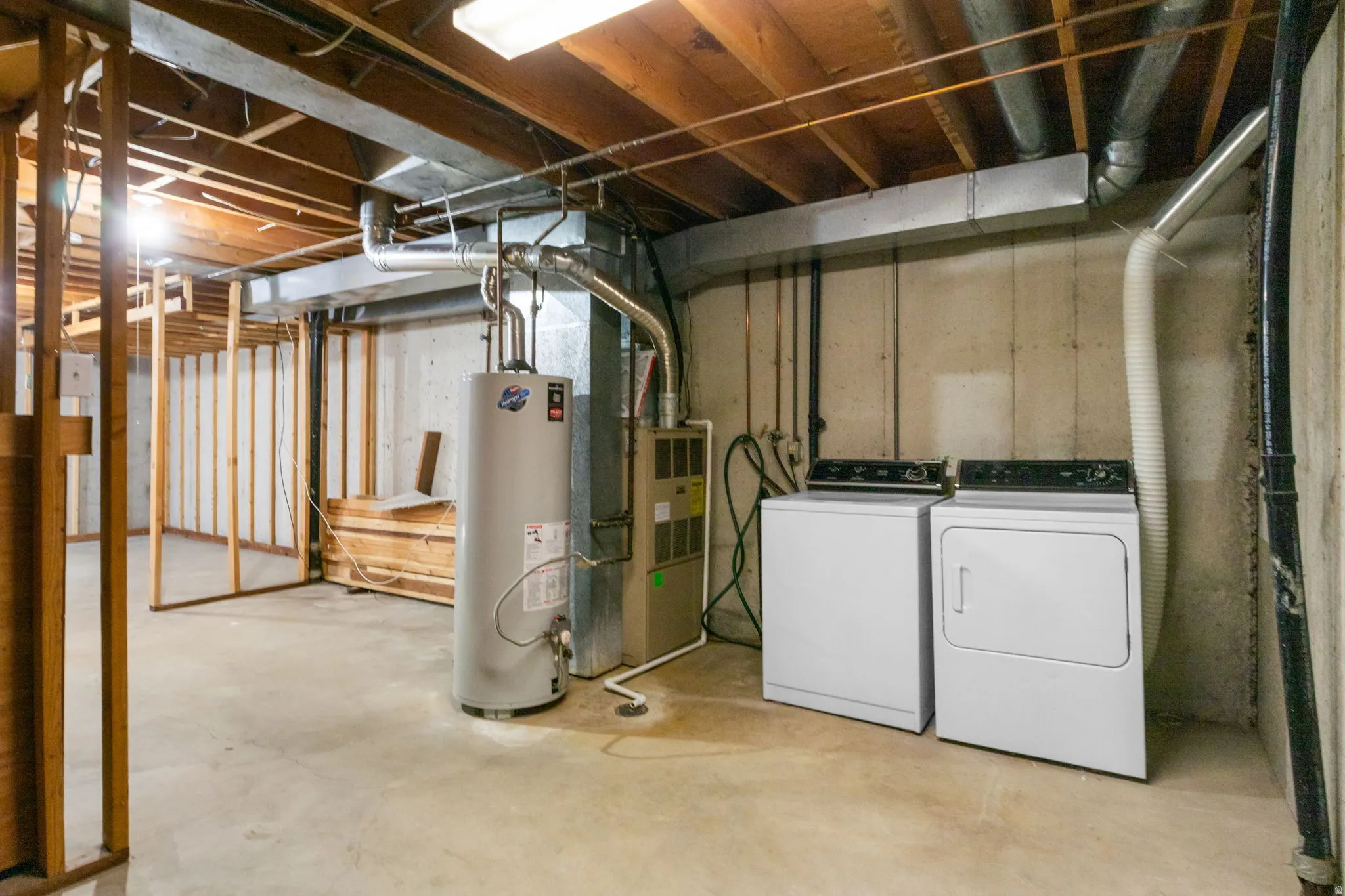 Unfinished basement space featuring exposed wooden ceiling joists, concrete flooring, and built-in laundry appliances