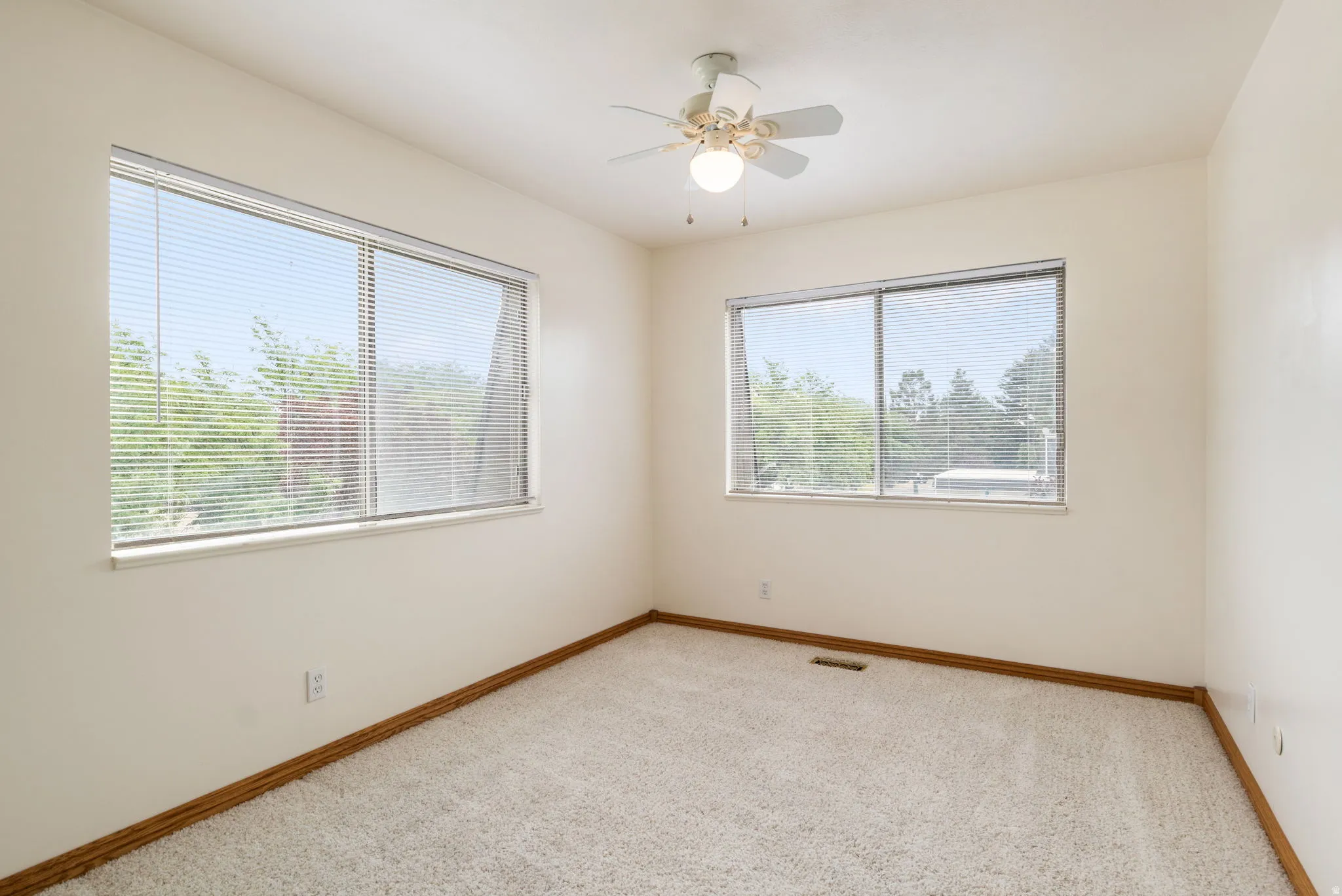 Spacious room featuring dual windows with blinds, light-toned carpeting, and a ceiling fan with integrated lighting
