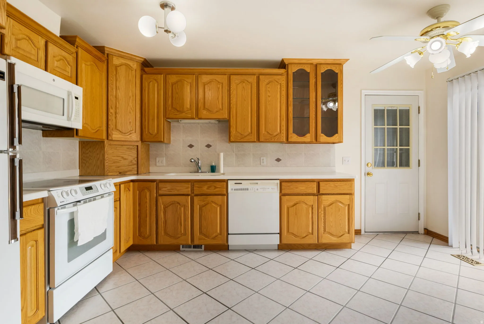 Kitchen featuring wood cabinetry, white appliances, light-toned countertops, and a full tile backsplash