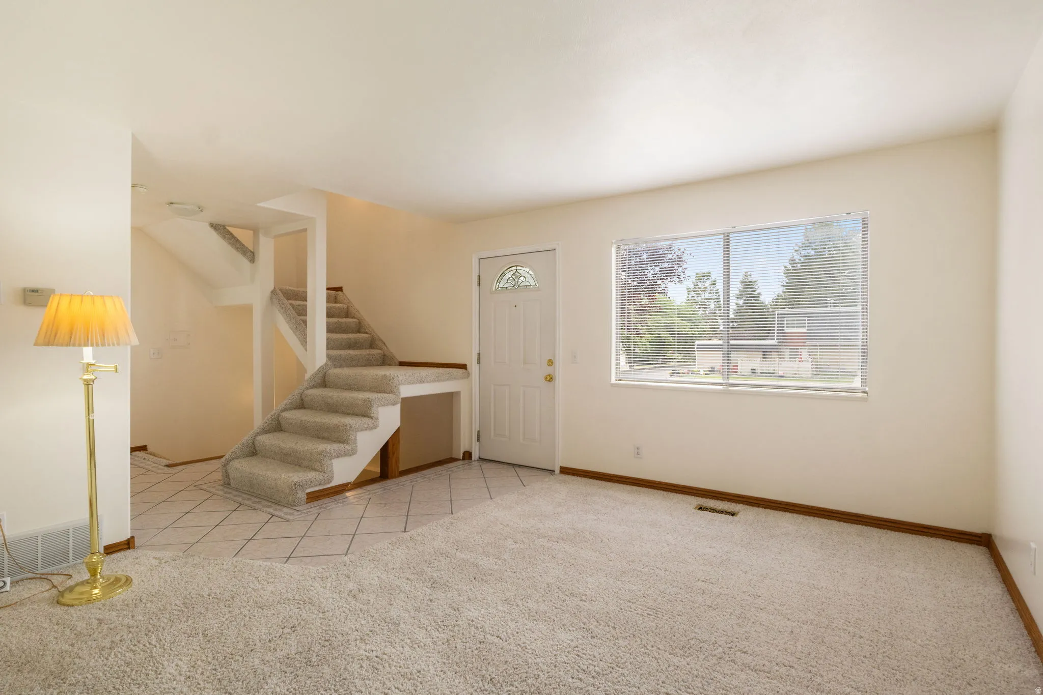 Spacious entry area featuring a carpeted staircase, a front door with a decorative glass insert, and a large window with blinds