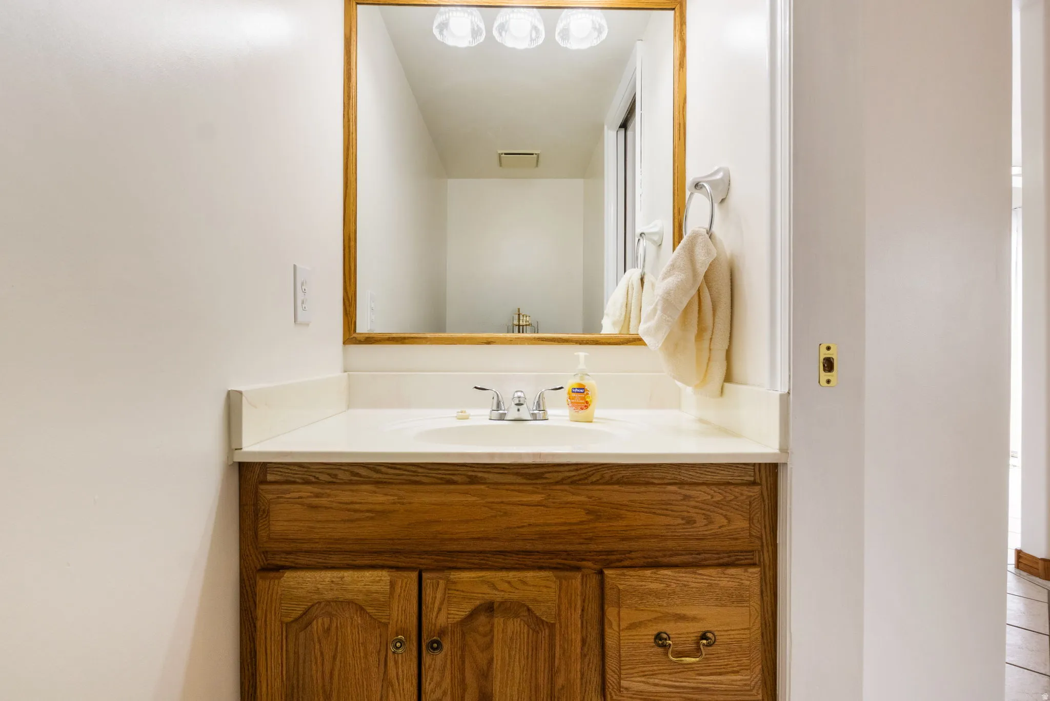 Vanity featuring a light wood-finish cabinet with brass hardware, a white countertop, and an integrated sink with a chrome faucet