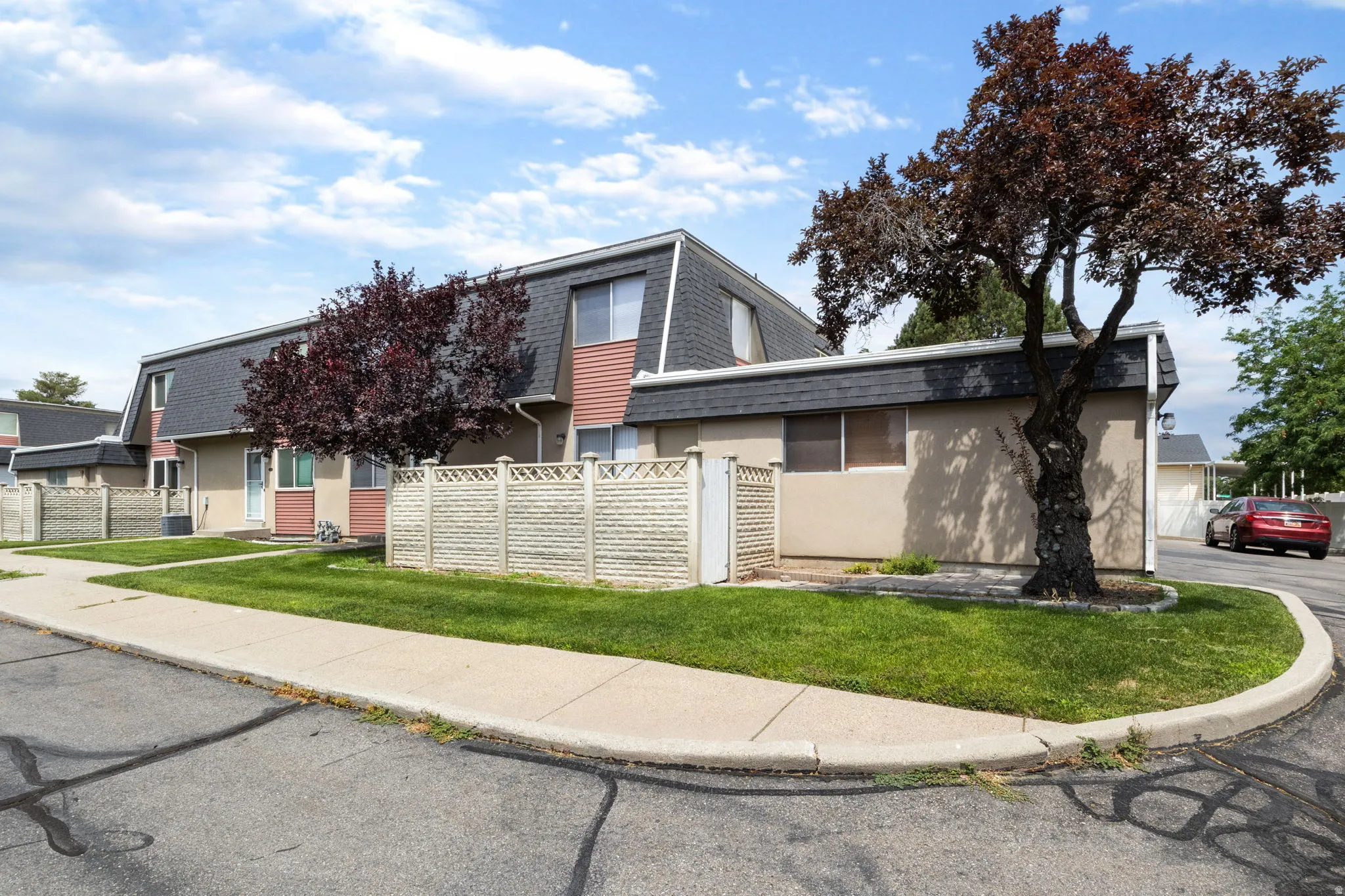 Townhome exterior featuring tan siding with red trim accents and a dark sloped roof