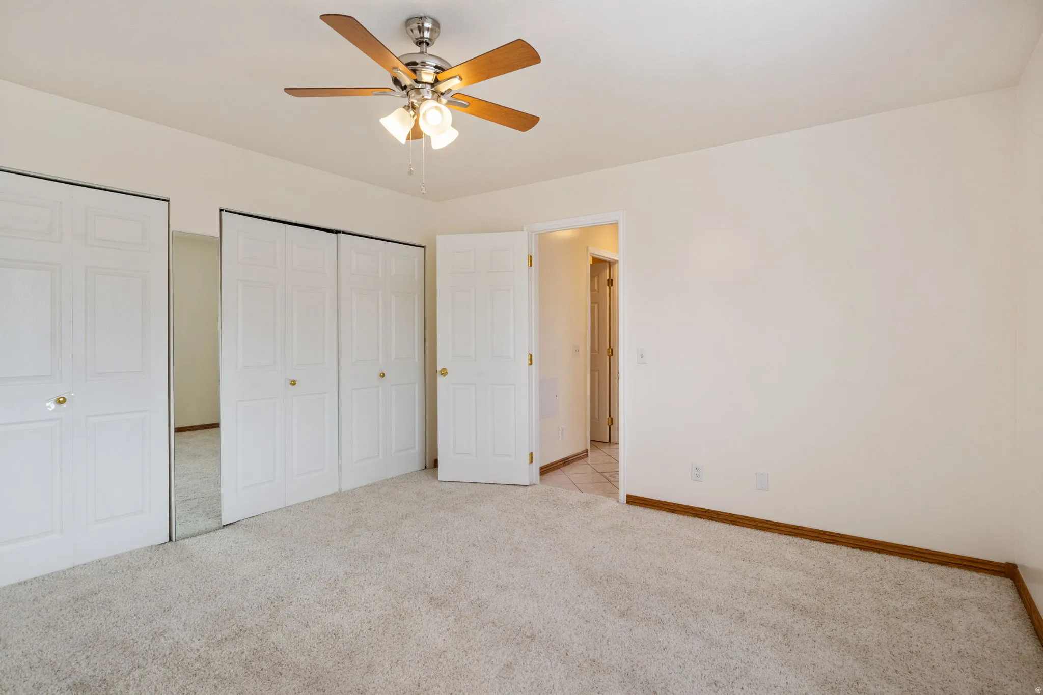 Carpeted room featuring a ceiling fan with light fixture, white bi-fold closet doors, and wood-finish trim
