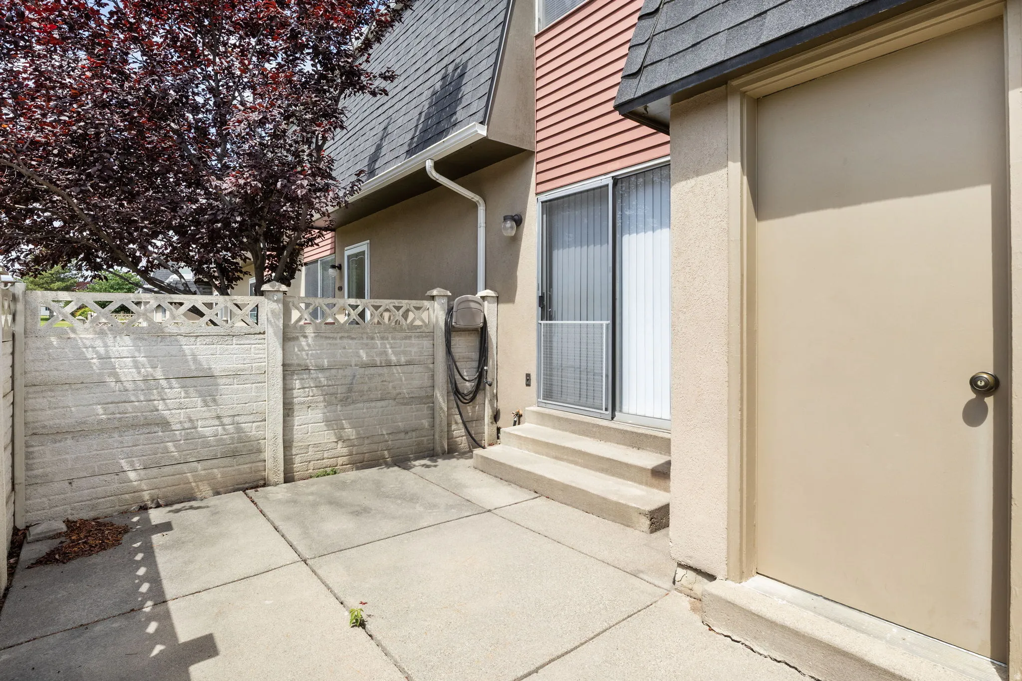 Exterior patio area featuring concrete paving, a decorative block fence, and mature foliage