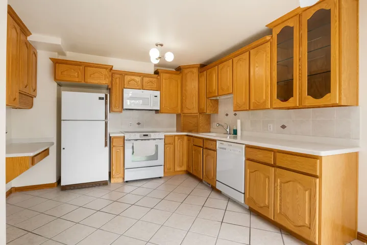 Kitchen featuring extensive wood cabinetry, white appliances, white countertops, tile backsplash, and tile flooring