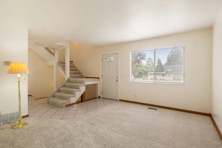 Spacious entry area featuring a carpeted staircase, a front door with a decorative glass insert, and a large window with blinds