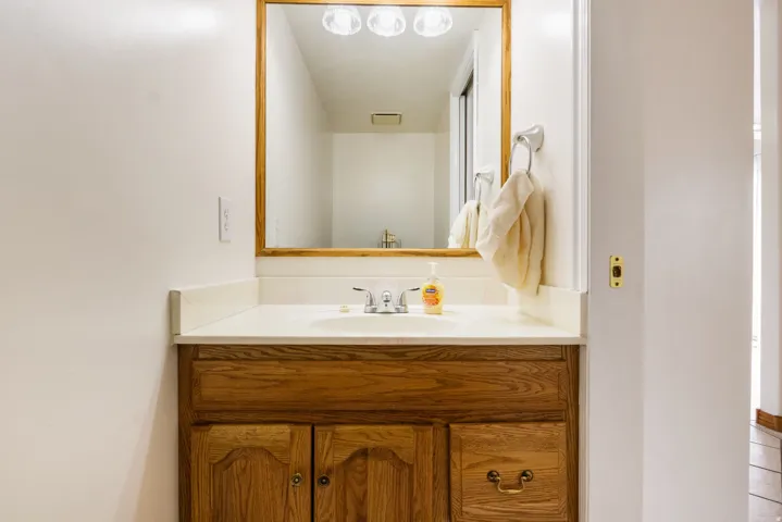 Vanity featuring a light wood-finish cabinet with brass hardware, a white countertop, and an integrated sink with a chrome faucet