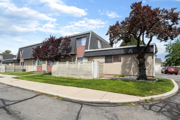 Townhome exterior featuring tan siding with red trim accents and a dark sloped roof