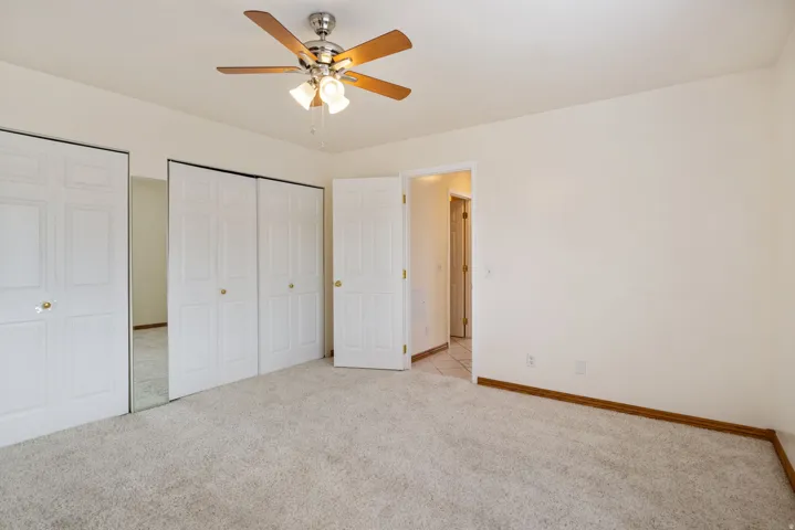 Carpeted room featuring a ceiling fan with light fixture, white bi-fold closet doors, and wood-finish trim