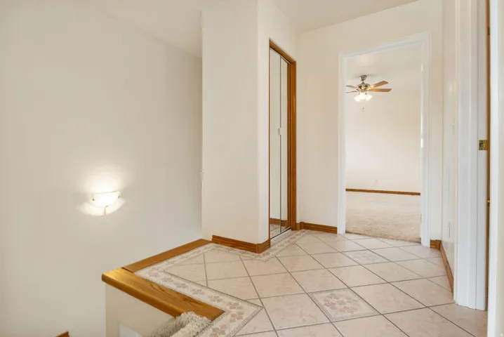 Tiled landing with decorative accents featuring a flush-mounted wall sconce, wood trim throughout, and a mirrored closet door