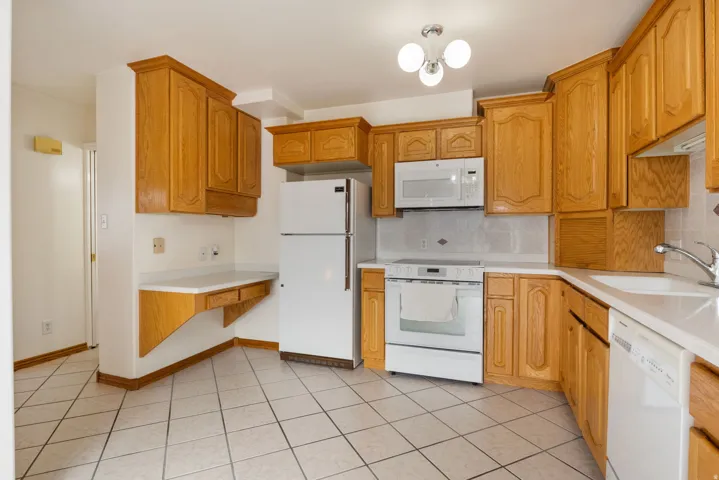 Kitchen featuring extensive wood cabinetry, white tile flooring, white countertops, built-in microwave, and a white electric range