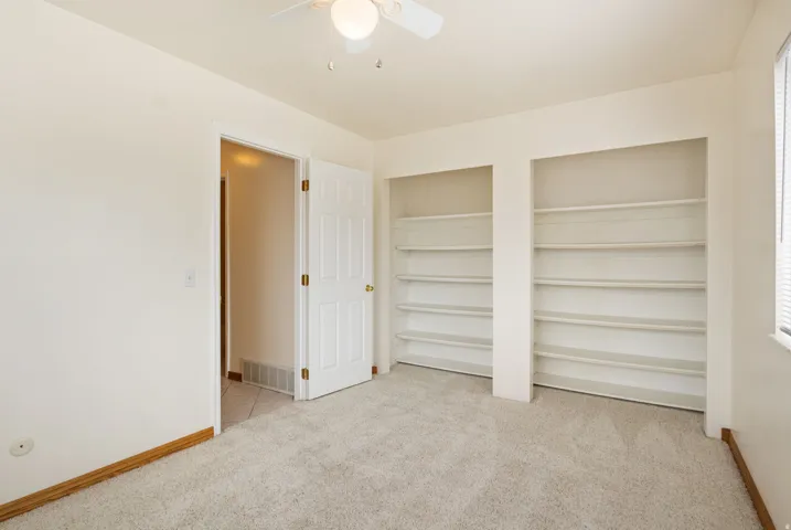 Carpeted room featuring two built-in shelving units, a ceiling fan with integrated lighting, and a window with blinds