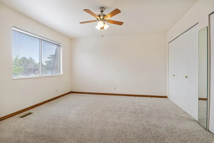 Carpeted room with a ceiling fan light fixture, large window with blinds, and white bi-fold closet doors, one featuring a mirrored panel