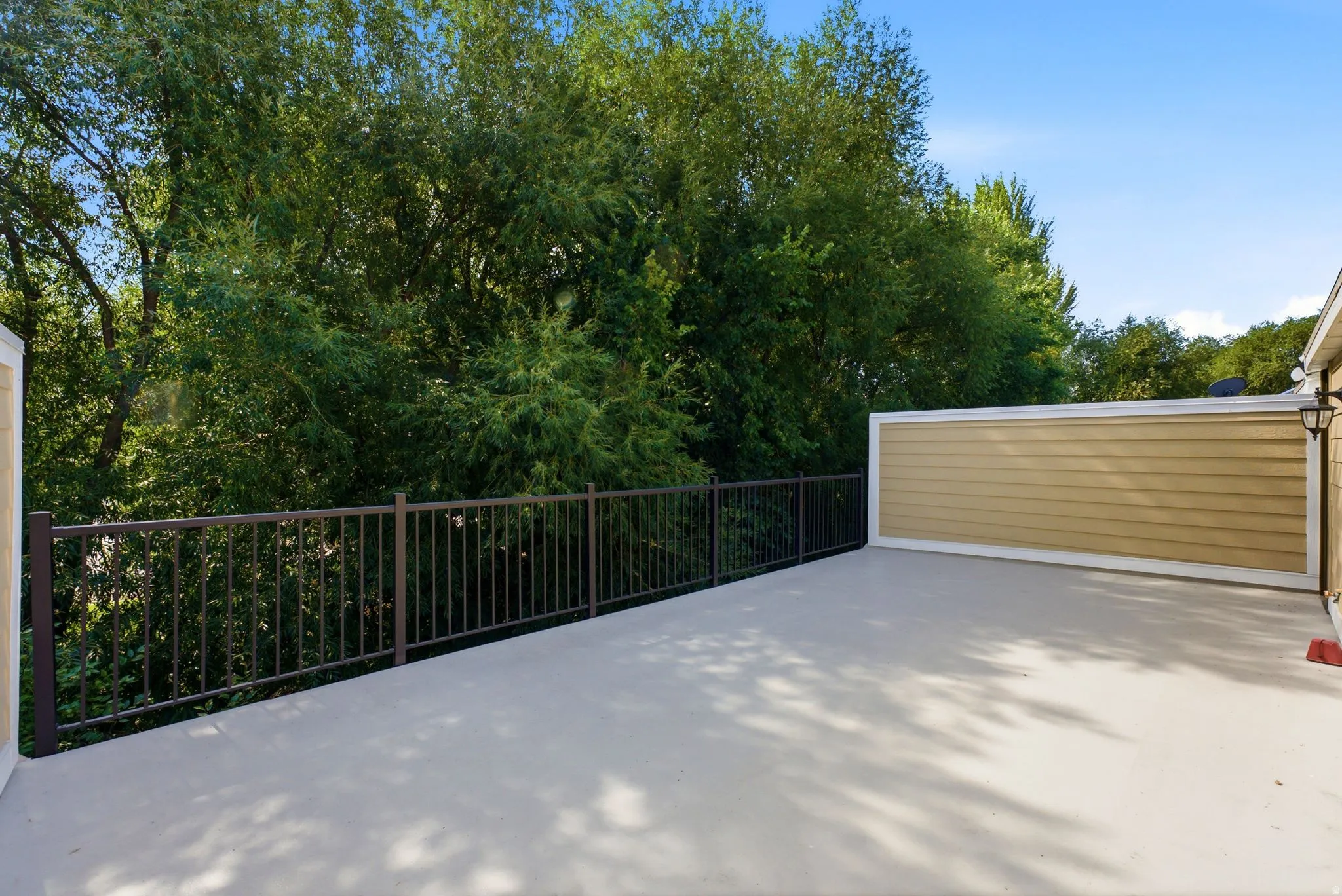 Spacious outdoor deck with concrete surfacing, featuring a dark bronze metal railing and surrounded by mature trees