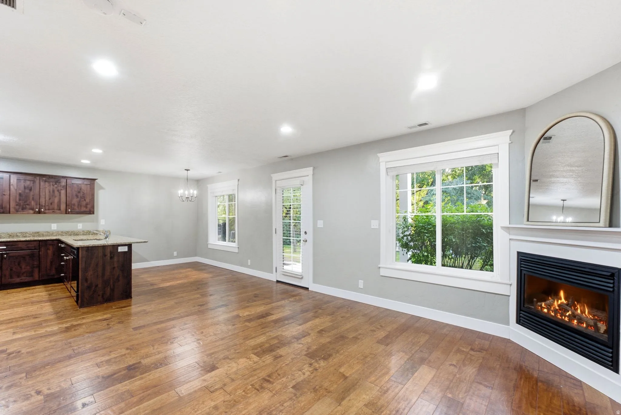 Open-concept living area featuring wood-finish flooring, a corner fireplace with a white mantel, and ample natural light from multiple windows