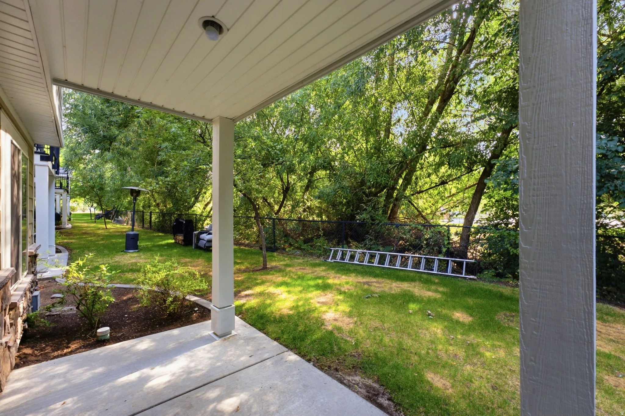 Covered patio with concrete flooring, supported by columns, offering access to the expansive lawn