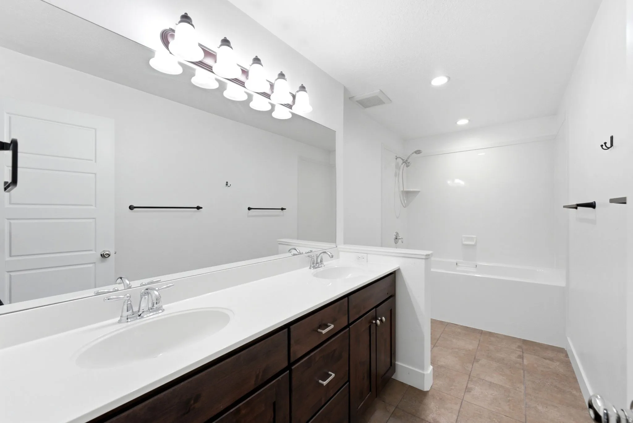 Bathroom featuring a double vanity with wood-finish cabinetry, a large mirror, a combined shower and soaking tub, and tile flooring