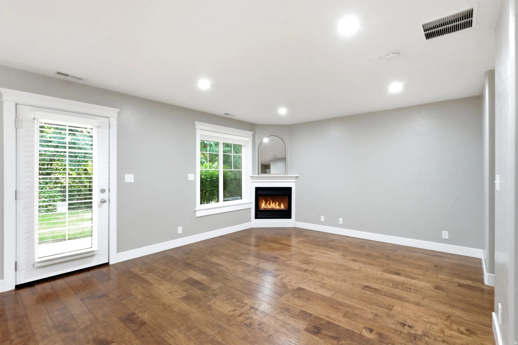 Spacious room featuring wood-finish flooring, a corner fireplace with a white mantel, and recessed lighting