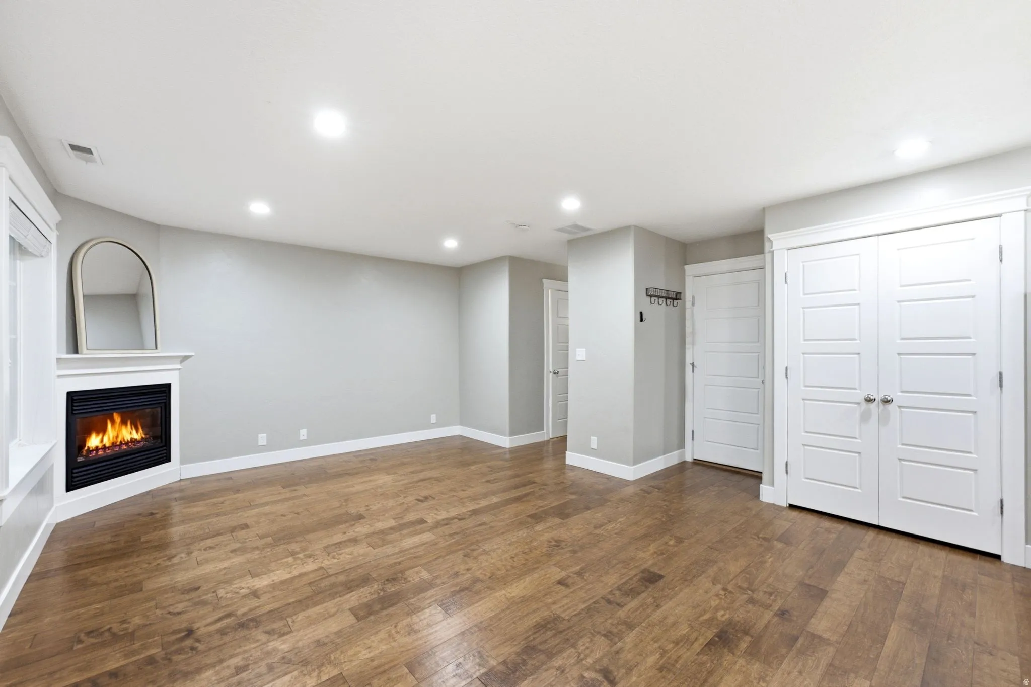 Spacious room featuring wood-finish flooring, a corner fireplace with white mantel, recessed lighting, and white bi-fold closet doors