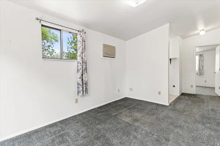 Carpeted interior space featuring white walls and a window with exterior tree views