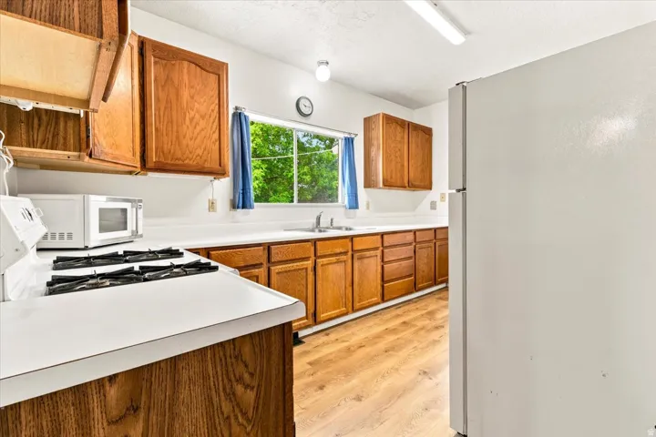 Kitchen featuring wood-finish cabinetry, white countertops, a four-burner gas range, a sink, and LVP flooring