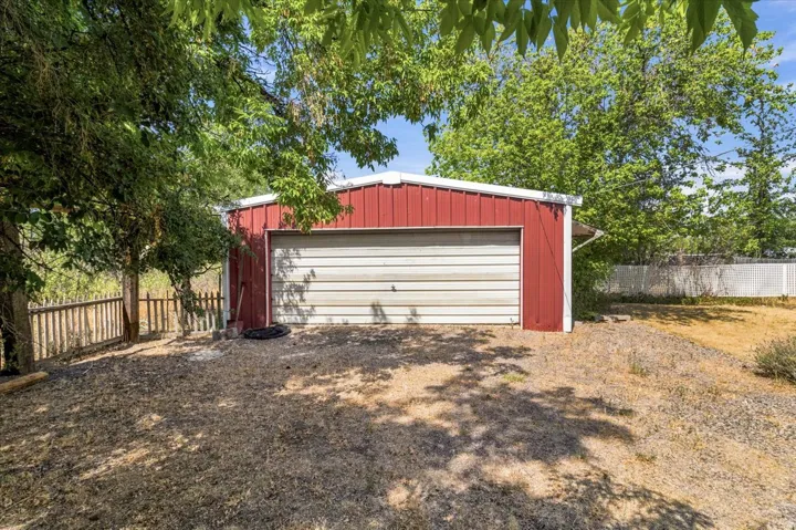 Red metal-sided outbuilding featuring a single garage door and white trim