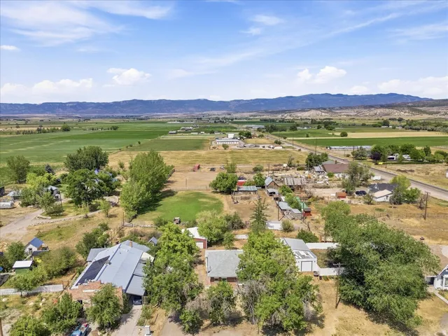 Expansive rural property featuring a main residence, surrounded by mature trees, a detached garage, and an open field backdrop with distant mountains