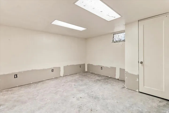 Unfinished interior space featuring a concrete floor, white painted walls, and two overhead rectangular fluorescent light fixtures